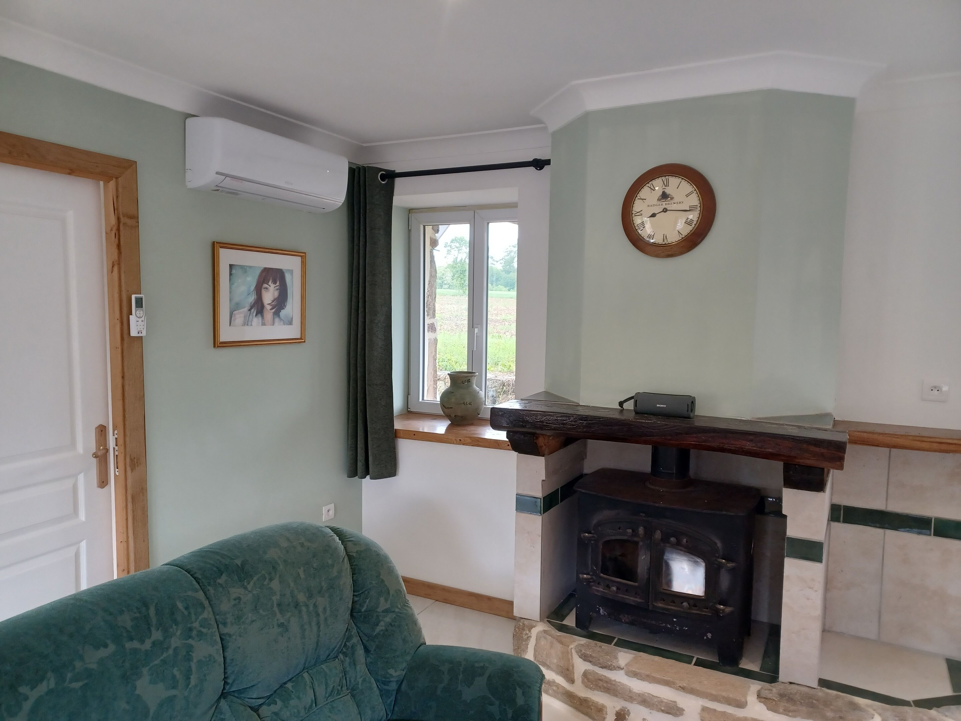 Una sala de estar con un sofá verde, una chimenea de piedra, un reloj y una ventana con cortinas.