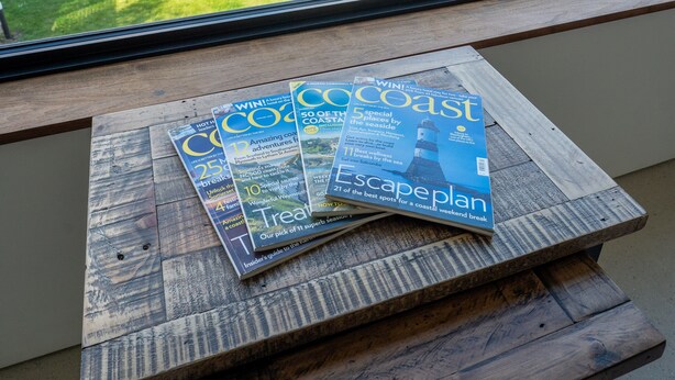 Een houten tafel met tijdschriften, met uitzicht op een groen landschap met heuvels.