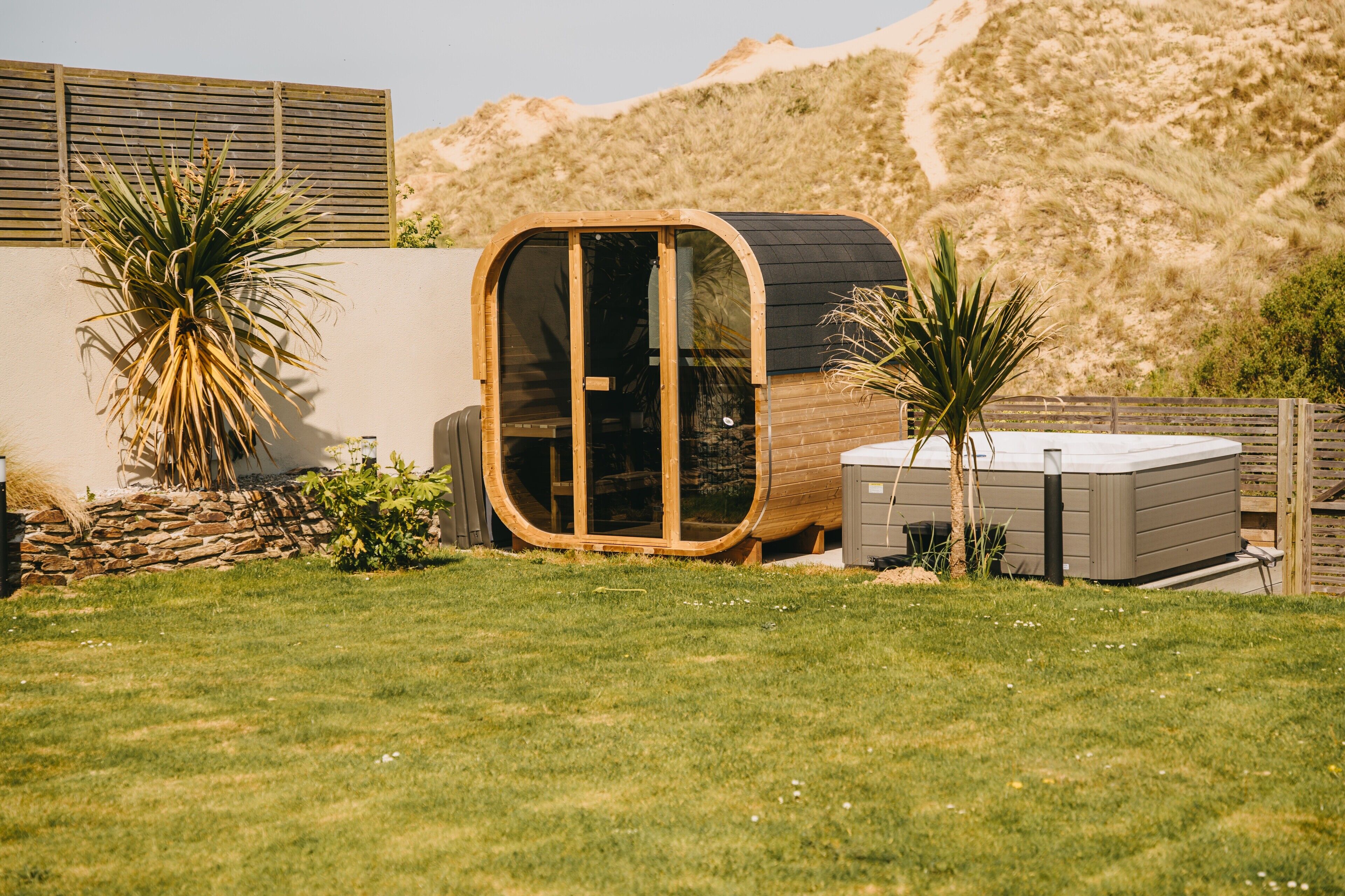 A modern, curved wooden structure with glass doors, surrounded by a well-maintained lawn and desert plants.