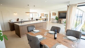 Een moderne keuken met een centraal eiland, een eethoek met een houten tafel en grijze stoelen, en een woonkamer met een bank en televisie.