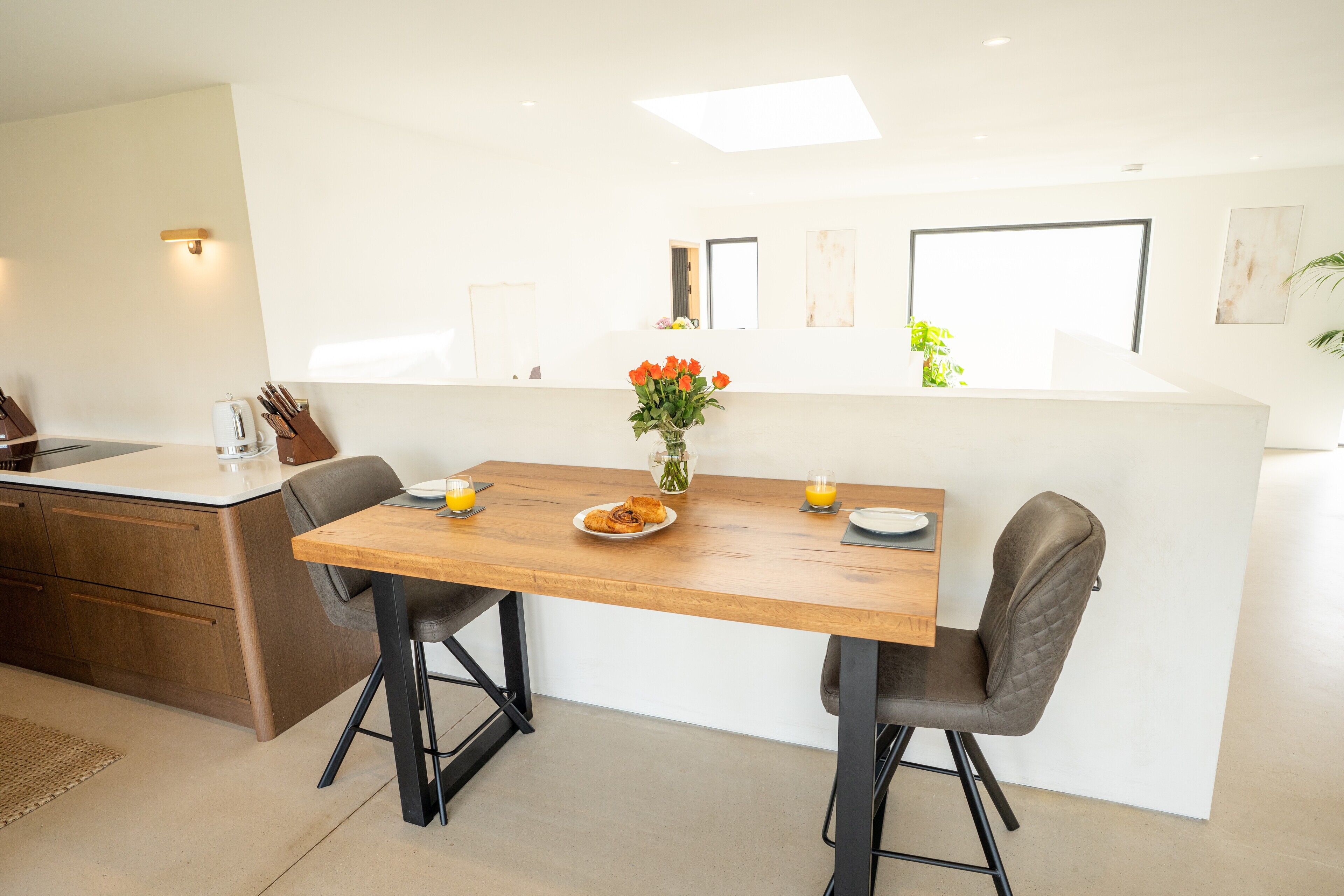 Eine moderne Küche mit einem Holztisch, zwei Stühlen, einer Blumenvase und einem gedeckten Frühstückstisch.