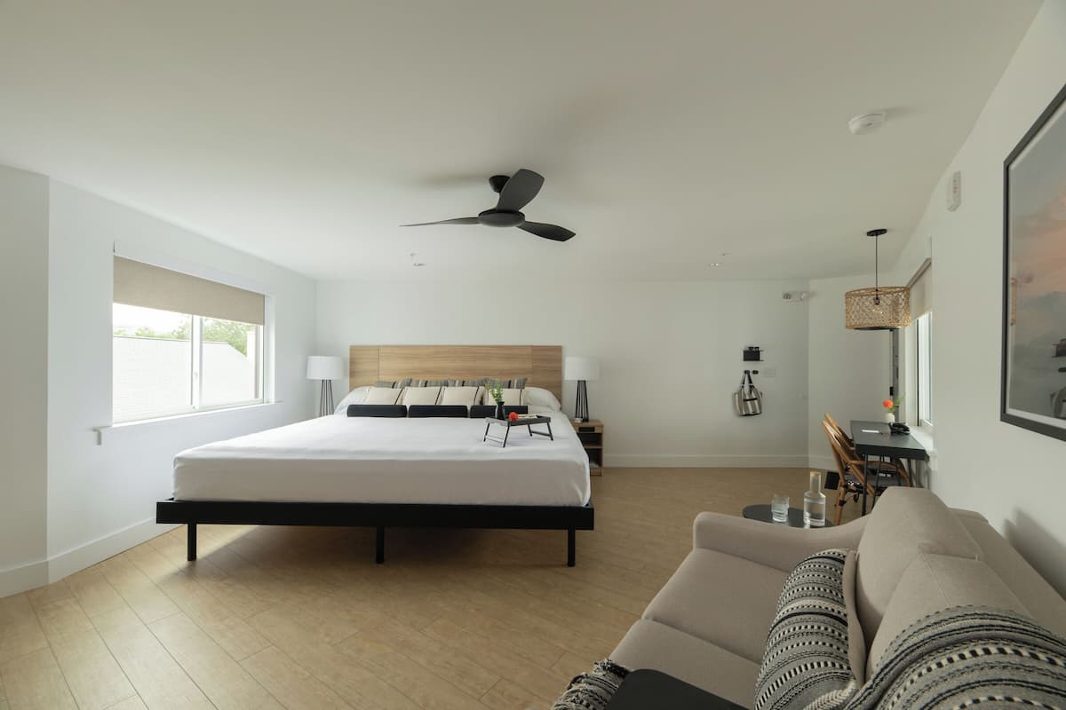 A modern bedroom with a large bed, a ceiling fan, a sofa, and a dining area.