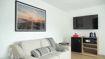 A modern living room with a sofa, a small table with glasses, a framed picture, a TV, and a mini-fridge.