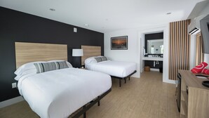 Ett hotellrum med två sängar, en sänggavel i trä, en tavla, ett skrivbord med en röd handduk och en spegel.