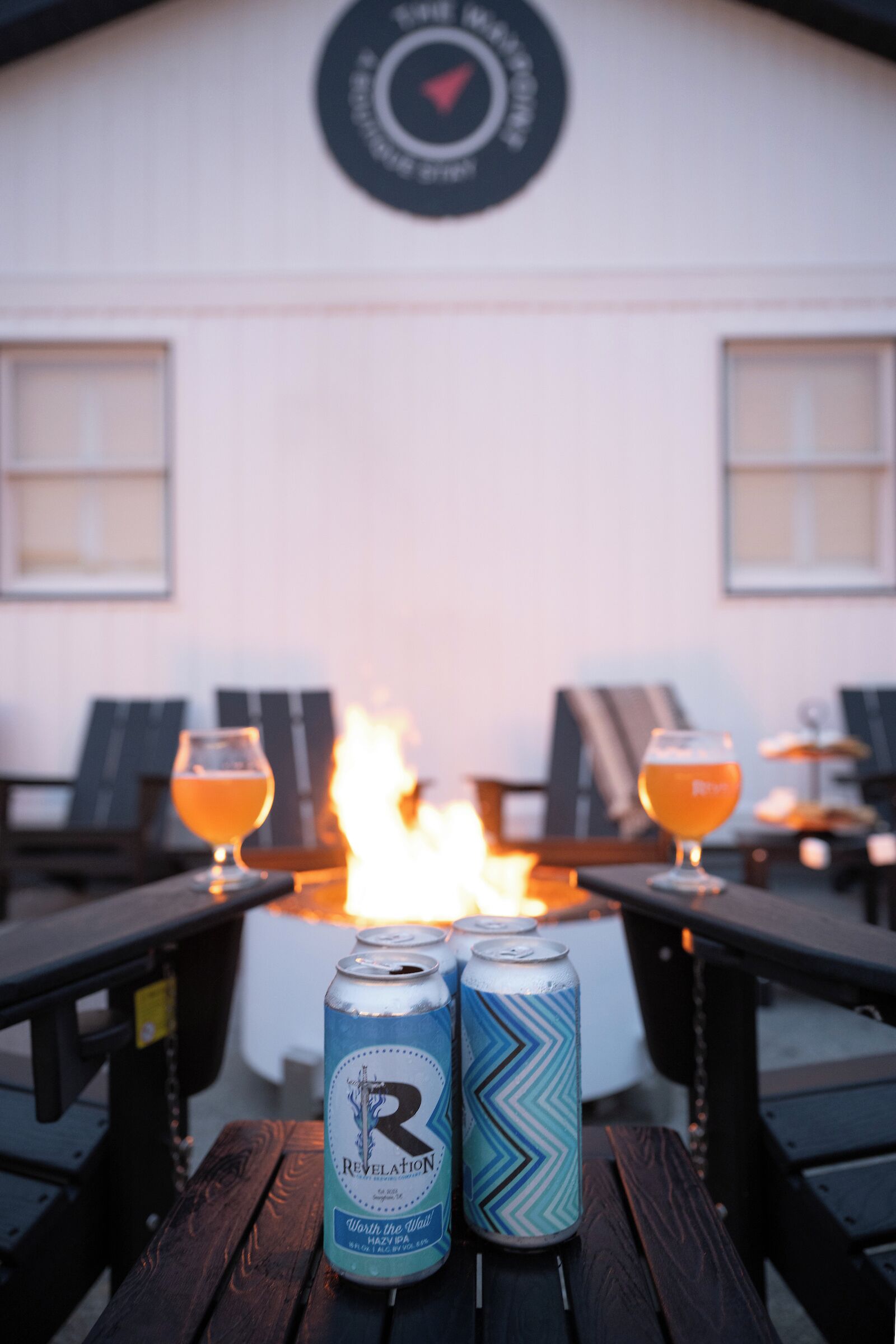 Une table avec deux canettes de bière Revelation et deux verres de bière, avec un feu en arrière-plan.
