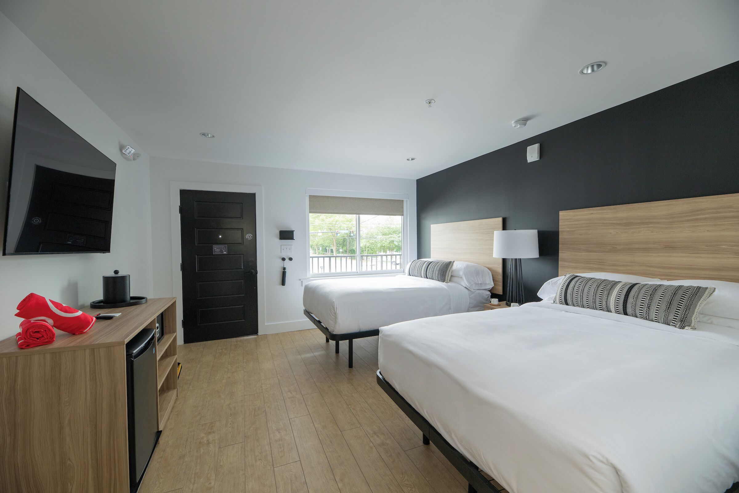 A hotel room with two beds, a wooden desk, a television, and a window with a view.