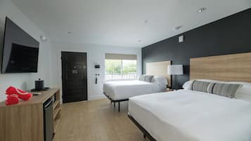 A hotel room with two beds, a wooden desk, a television, and a window with a view.