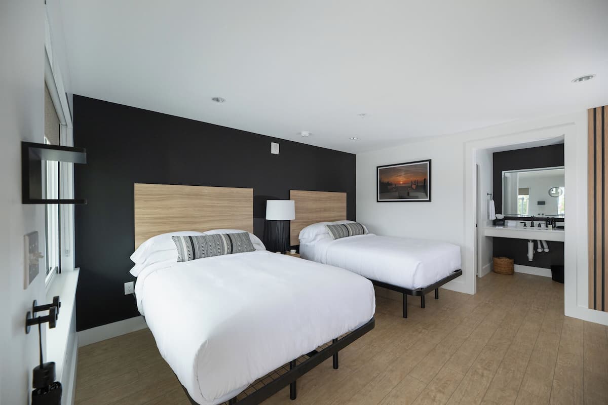 A modern hotel room with two beds, a large mirror, and a view of the cityscape.