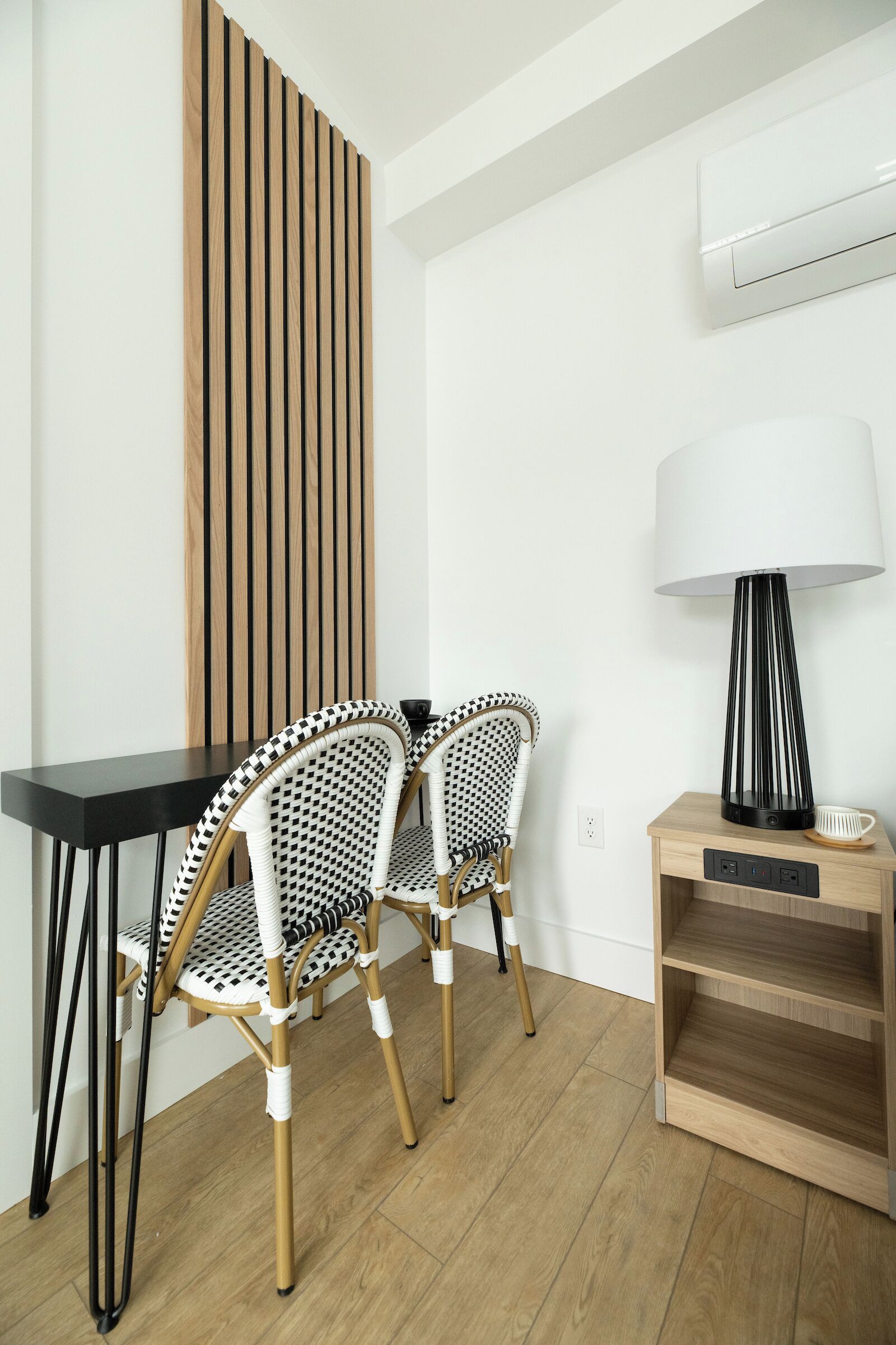A modern room with a black table, two patterned chairs, a wooden sideboard, and a floor lamp.