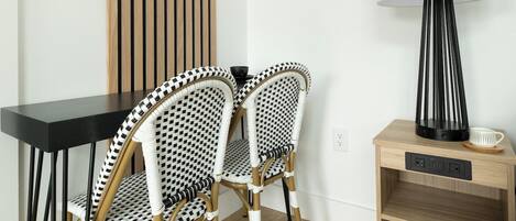 A modern room with a black table, two patterned chairs, a wooden sideboard, and a floor lamp.