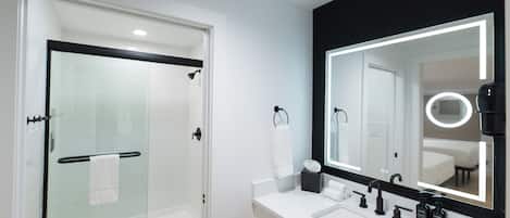 A modern bathroom with a glass shower enclosure, a white sink with black fixtures, and a large mirror with integrated lighting.