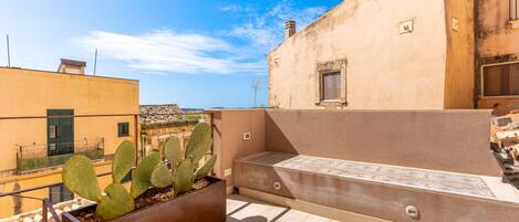 A rooftop terrace with a cactus planter, a tiled bench, and a view of the cityscape.