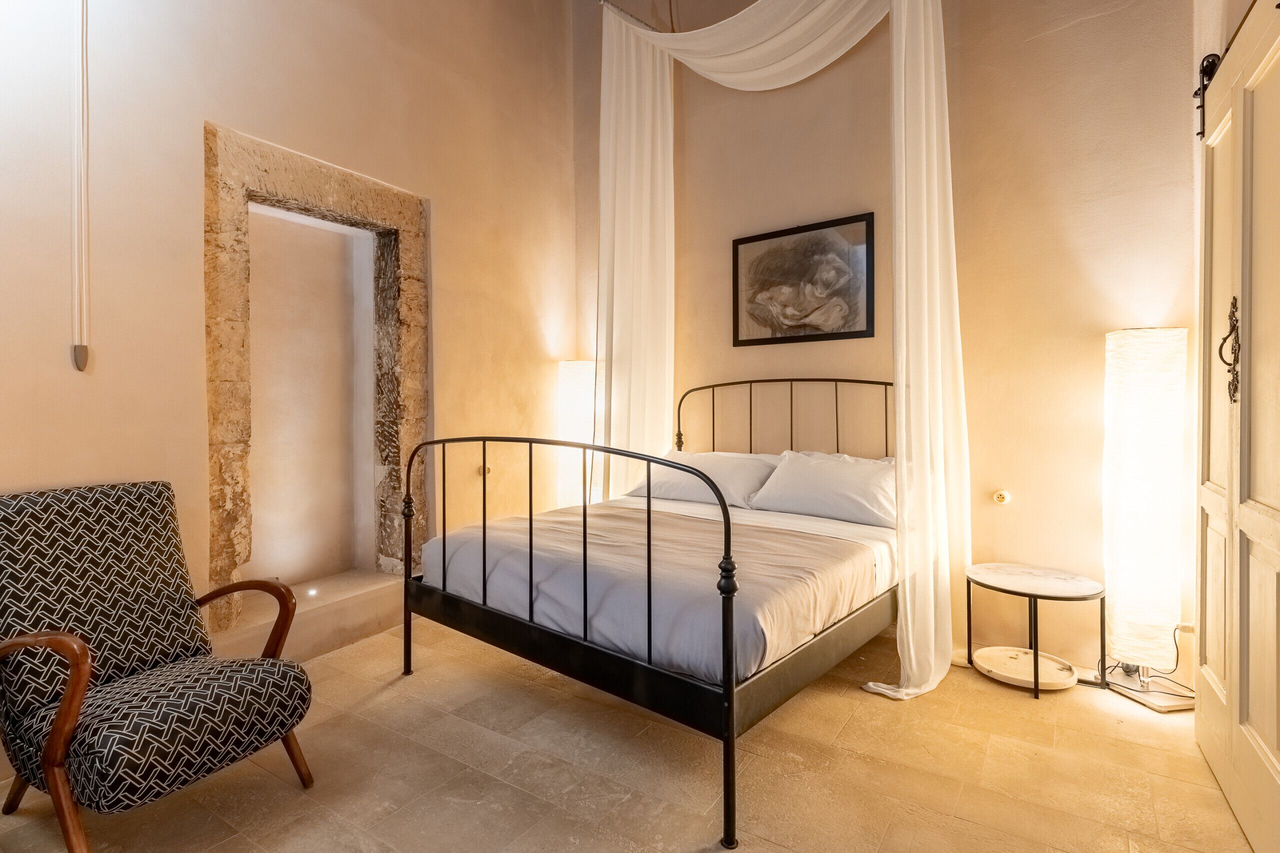 A bedroom with a bed, a chair, a small table, and a painting on the wall.