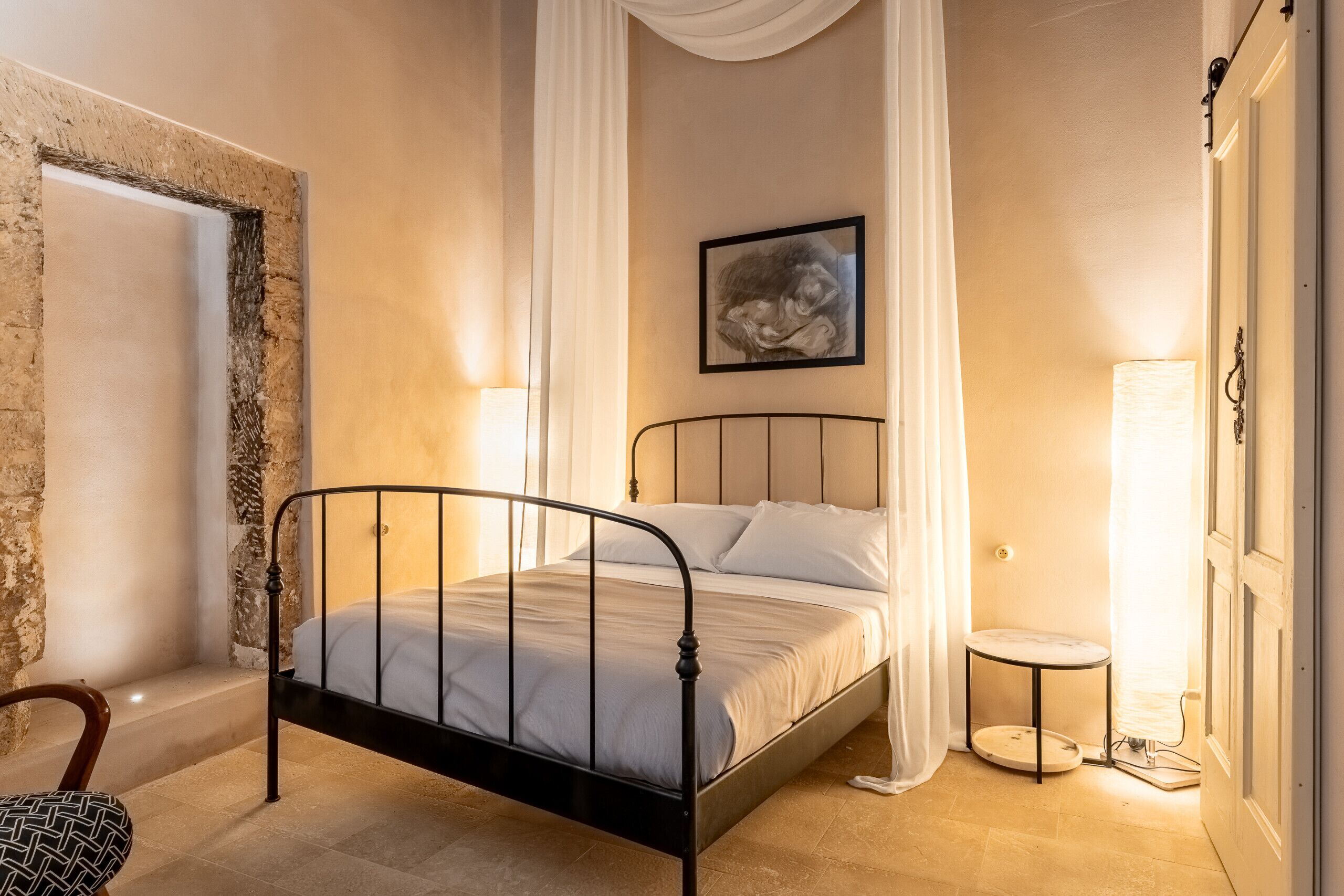 Quarto com cama, uma cadeira, mesa de cabeceira e quadro na parede.
