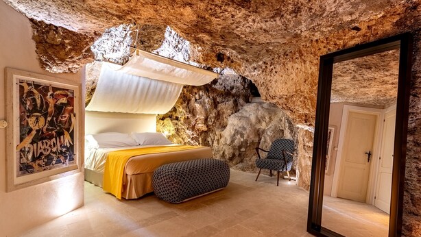 Quarto com cama, poltrona, espelho grande e parede que lembra uma gruta.