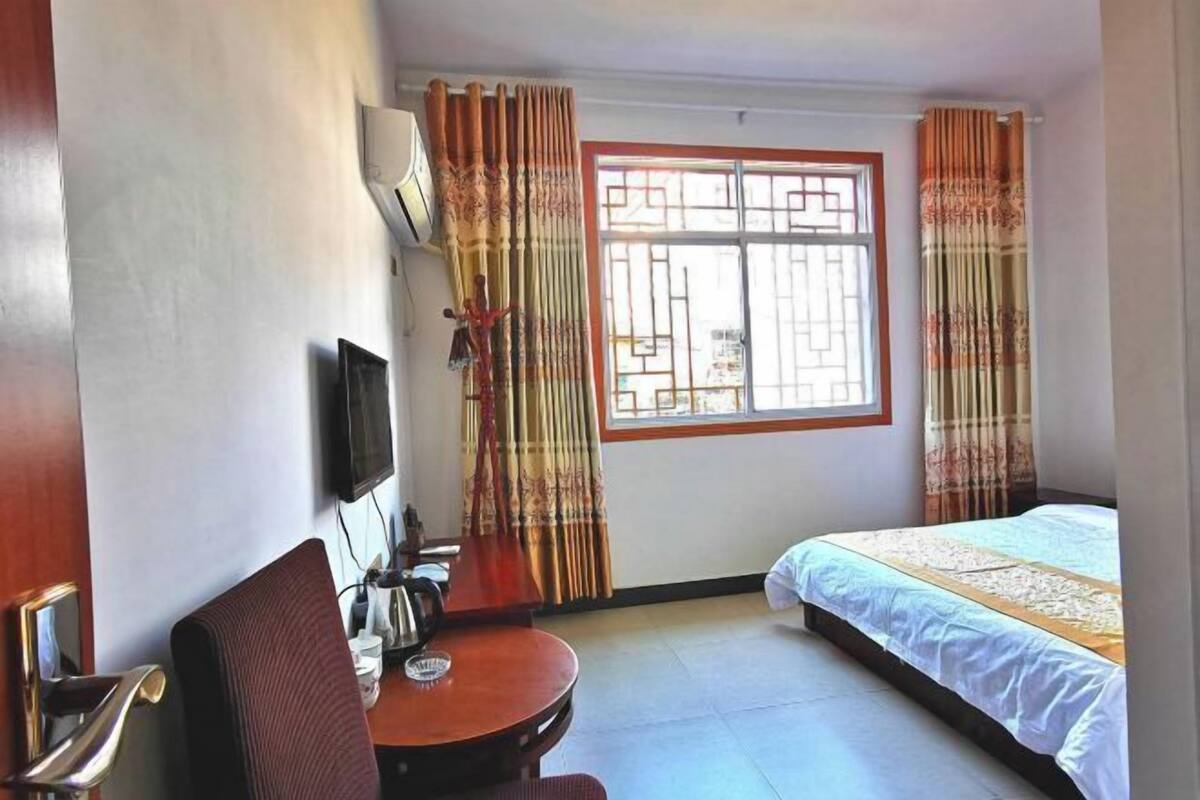 A hotel room with a bed, a desk with a chair, a TV mounted on the wall, and a window with curtains.