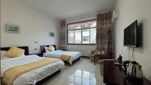 A hotel room with two beds, a TV, a desk with a kettle, and a window with curtains.
