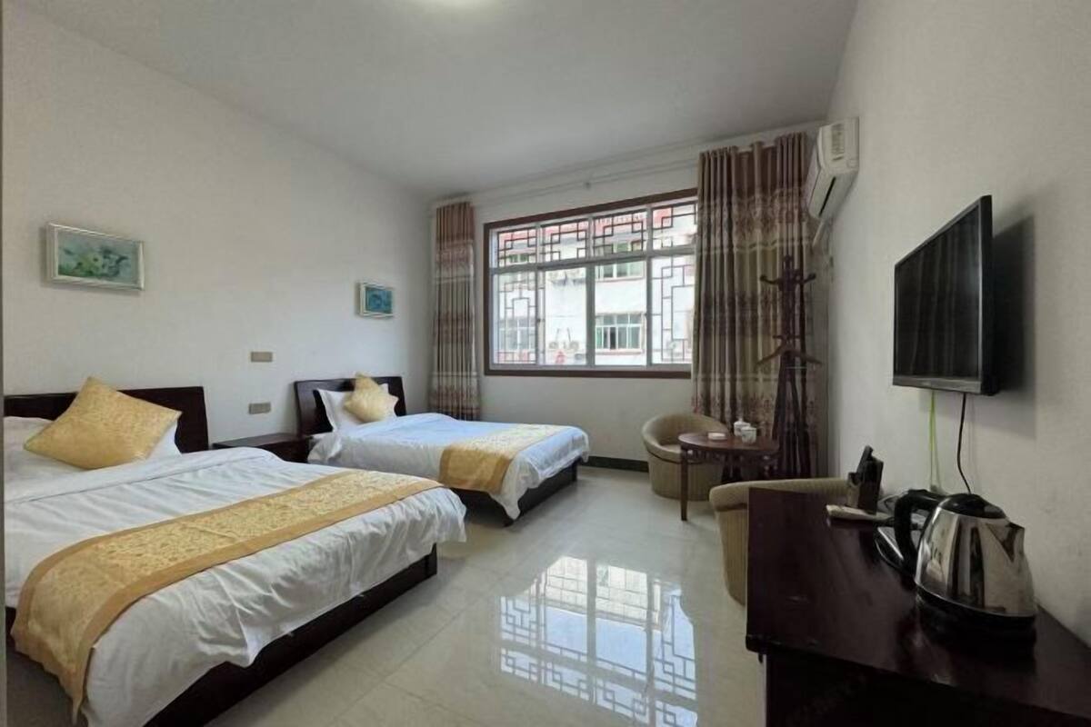 A hotel room with two beds, a TV, a desk with a kettle, and a window with curtains.
