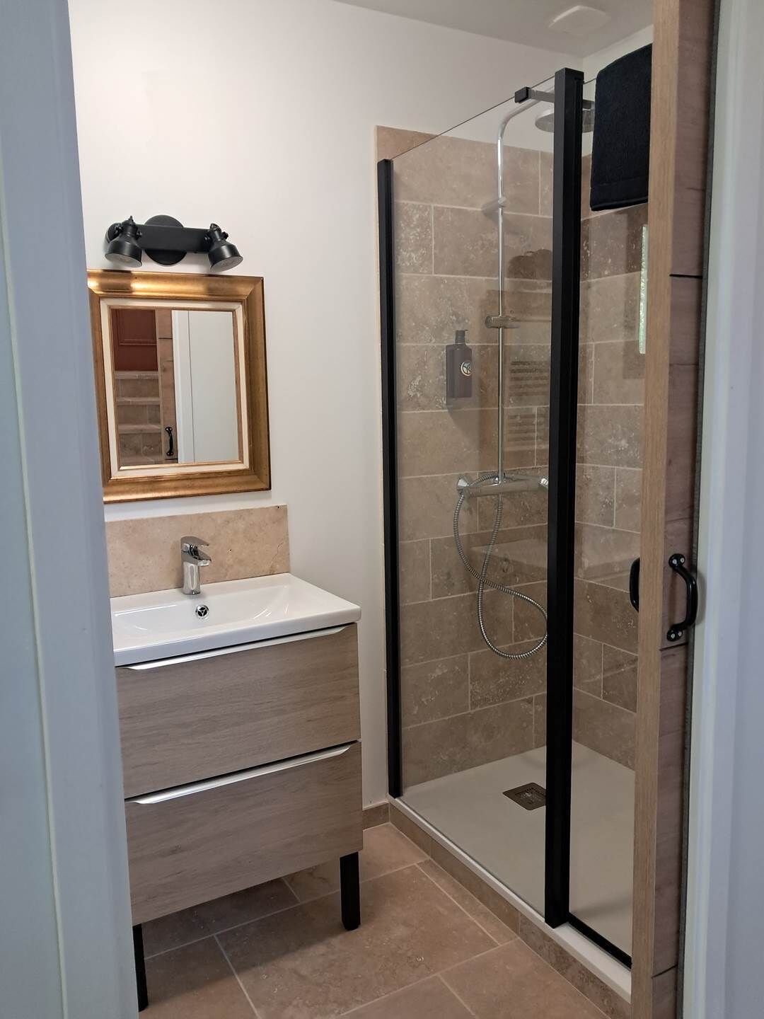 A modern bathroom with a glass shower enclosure, a sink with a mirror above it, and a wooden vanity.