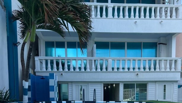 A pool area with a two-story building, a palm tree, and a blue-tiled pool. - HNH HOTEL LUXURY EXPERIENCE VIP (San Andrés)