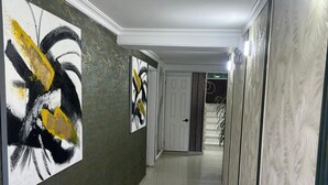 A hallway with abstract paintings on the walls, a white door at the end, and a patterned wall on the right. - HNH HOTEL LUXURY EXPERIENCE VIP (San Andrés)