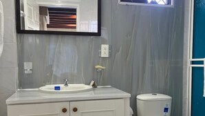 A bathroom with a white vanity, a mirror, a toilet, and a window with a view of the outside. - HNH HOTEL LUXURY EXPERIENCE VIP (San Andrés)