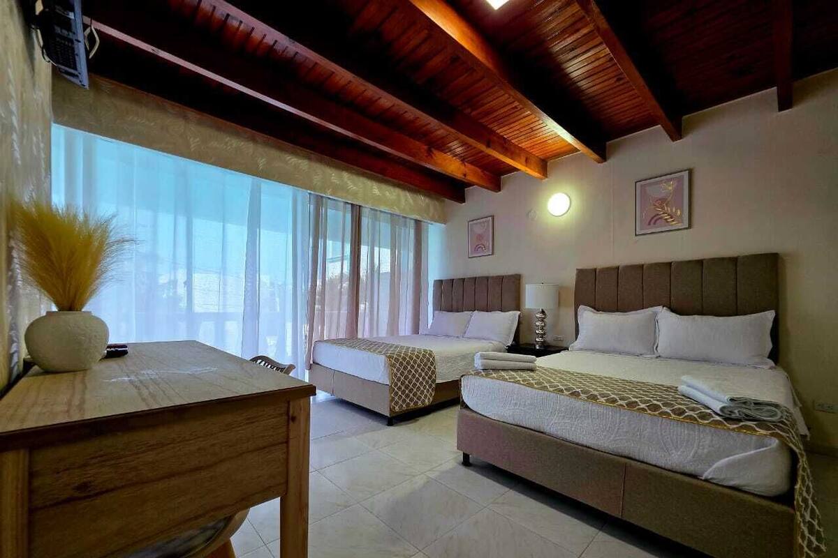 Une chambre d’hôtel avec deux lits, un bureau en bois et une grande fenêtre avec des rideaux.