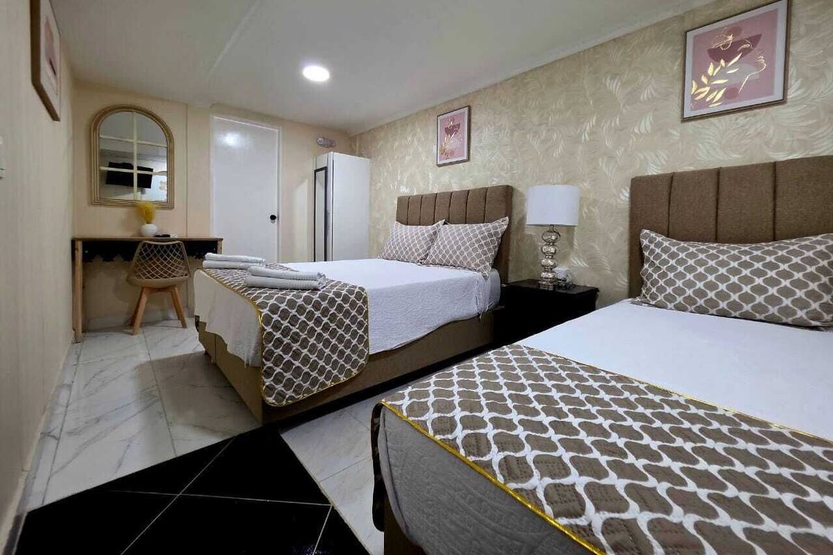 Une chambre d’hôtel avec deux lits, un bureau, une chaise, un miroir et un réfrigérateur.