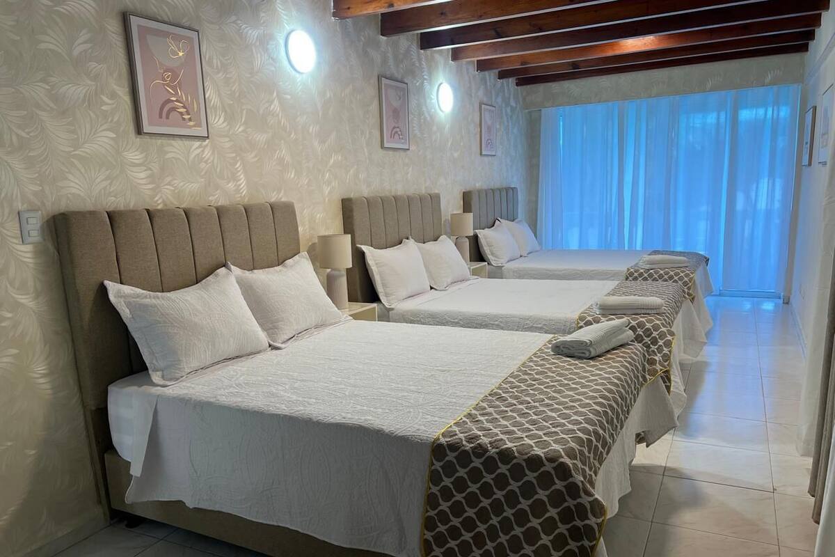 Une chambre d’hôtel avec deux lits, chacun doté d’une tête de lit et d’oreillers, une fenêtre avec des rideaux et un plafond en bois.