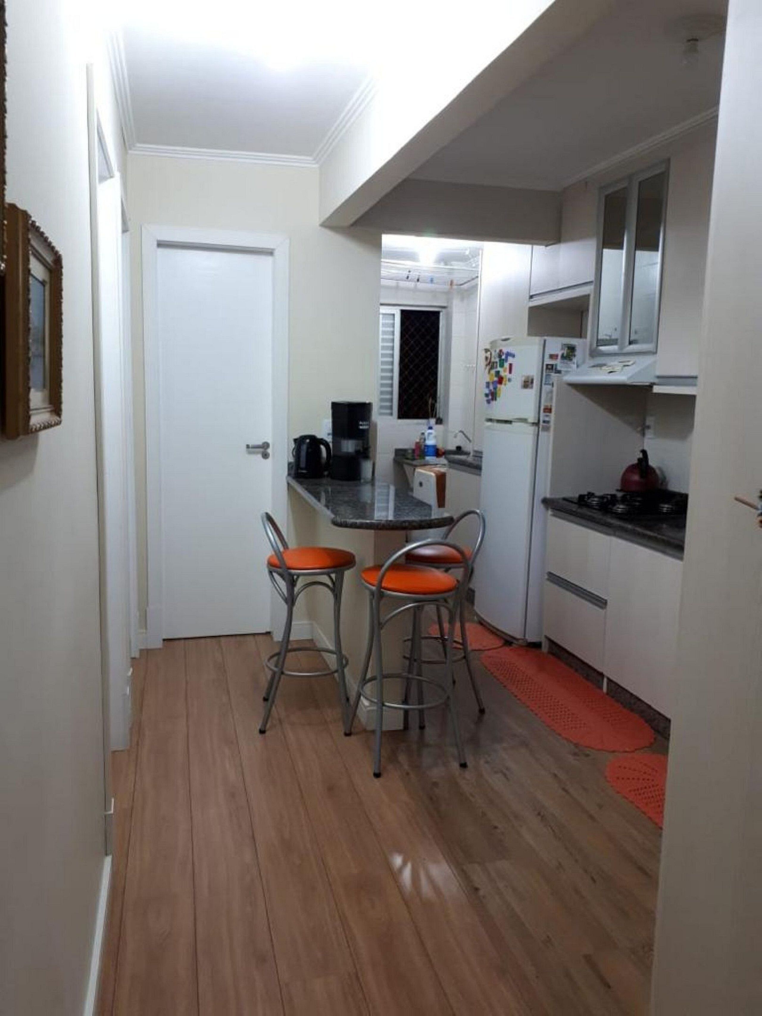 Cocina compacta con comedor, armarios blancos, refrigerador, estufa y dos taburetes de bar.