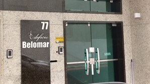A hotel entrance with a glass door, a keypad lock, and a sign indicating a protected area. - Ap Beira Mar - Ed Belo Mar - BC (Balneario Camboriu)