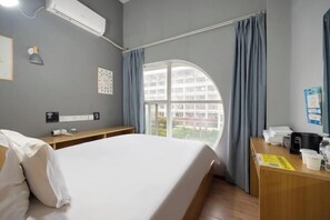 A hotel room with a bed, a desk with a telephone, a window with curtains, and a wall-mounted air conditioner. - yun jing Hotel (Shanghai Songjiang University Town) (Shanghai)