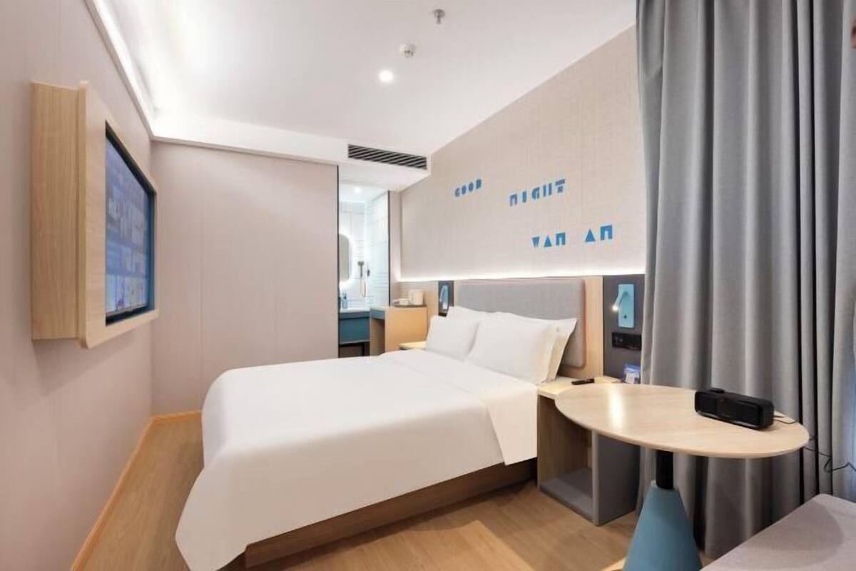 Ein modernes Hotelzimmer mit einem großen Bett, einem kleinen Tisch und einem an der Wand befestigten Fernseher.