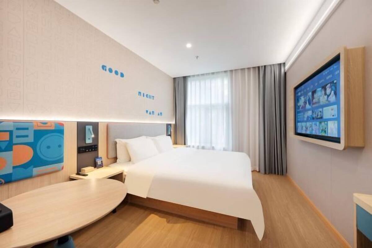 Ein Hotelzimmer mit einem großen Bett, einem Schreibtisch, einem an der Wand befestigten Fernseher und einem Fenster mit Vorhängen.