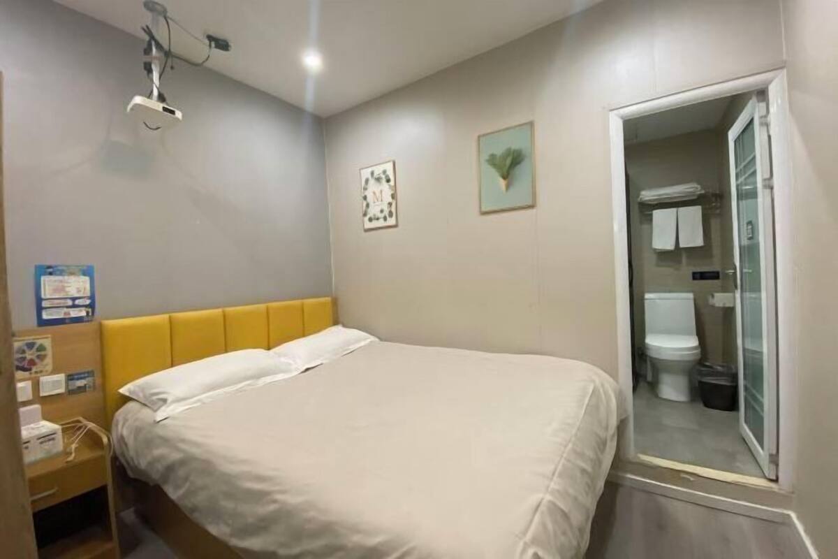 Ein Hotelzimmer mit Bett, Nachttisch mit Lampe, einem gerahmten Bild an der Wand und angrenzendem Badezimmer.