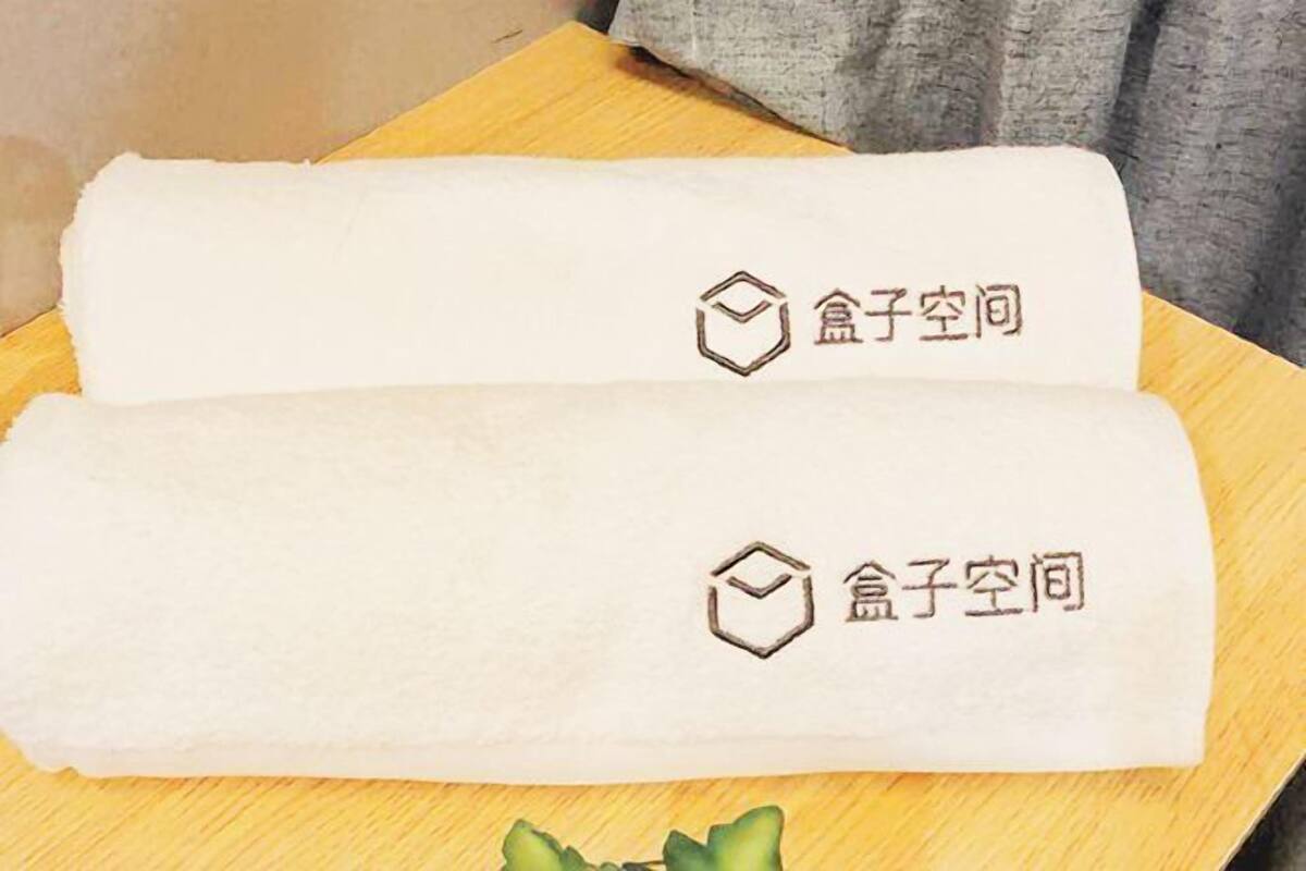 Zwei zusammengerollte Handtücher mit Logo und Schriftzug auf einer Holzfläche.