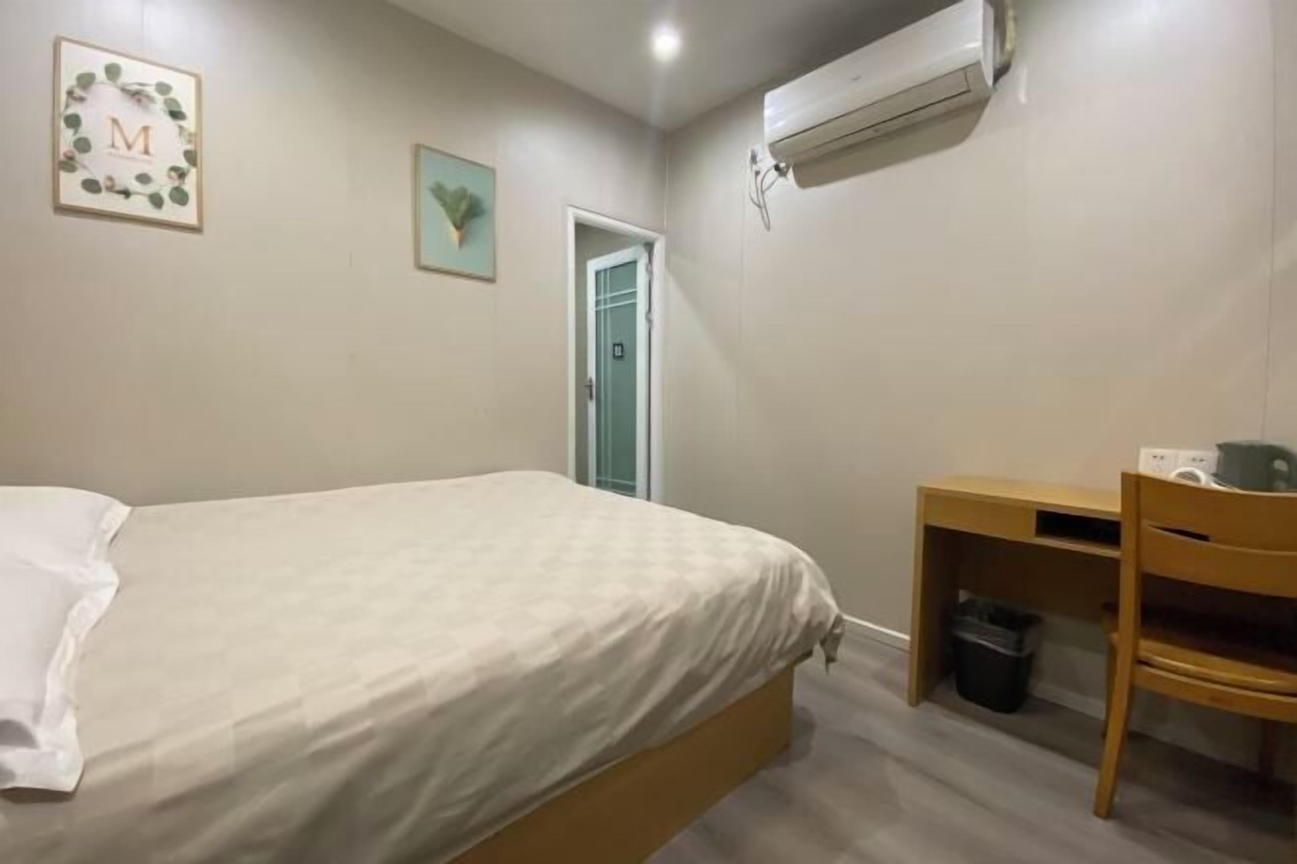 A bedroom with a bed, a desk, a chair, and a trash bin.