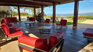 A covered outdoor seating area with red cushioned chairs and a wooden table, overlooking a pool and lush greenery. - Apartment Costa Rica Santa Ana Avalon Country club gym, swimming pool tennis. (Río Oro)
