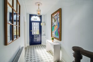 Ein Flur mit einer blauen Tür, einem weißen Konsolentisch mit Pflanze und einem farbenfrohen Gemälde an der Wand.