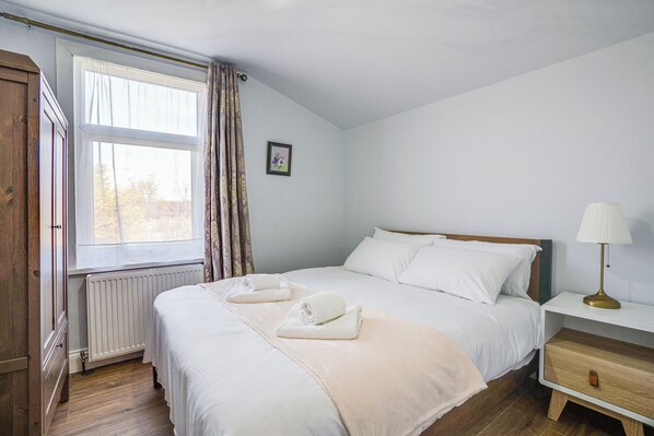 Ein Schlafzimmer mit Bett, Nachttisch mit Lampe, Heizkörper und einem Fenster mit Vorhängen.