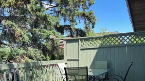 A wooden deck with a table and chairs, a wooden fence, and a tree in the background.