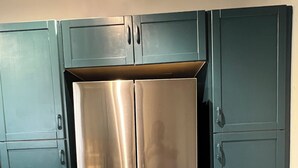 A stainless steel refrigerator in a kitchen with teal cabinetry and a wooden floor.