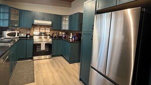 A modern kitchen with teal cabinets, stainless steel appliances, and a wooden ceiling.