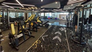 A modern gym with various exercise equipment, a marble floor, and a large mirror reflecting the space.