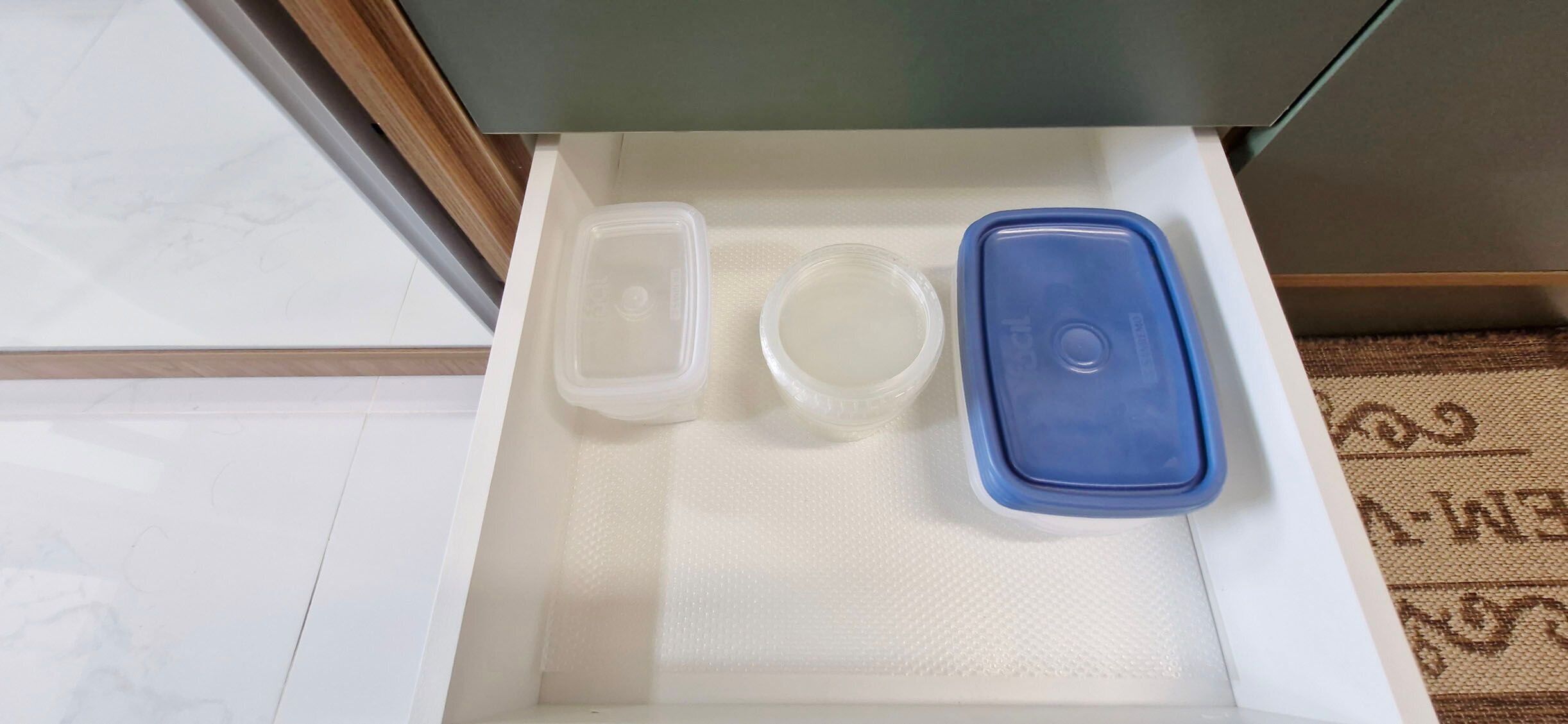 A drawer with a white mat, a blue container, and a clear container.