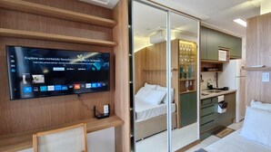 A modern room with a TV, a bed, a small kitchenette, and a sliding door leading to another room. - COARM0102 - Smart Convenções (Salvador)