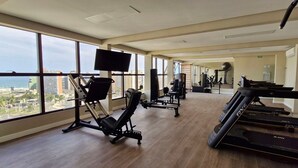 A gym with treadmills, a rowing machine, and weight machines, large windows with a city view. - COARM0102 - Smart Convenções (Salvador)