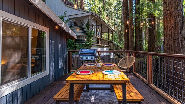 Une terrasse en bois avec une table et des chaises, un barbecue et des guirlandes lumineuses.