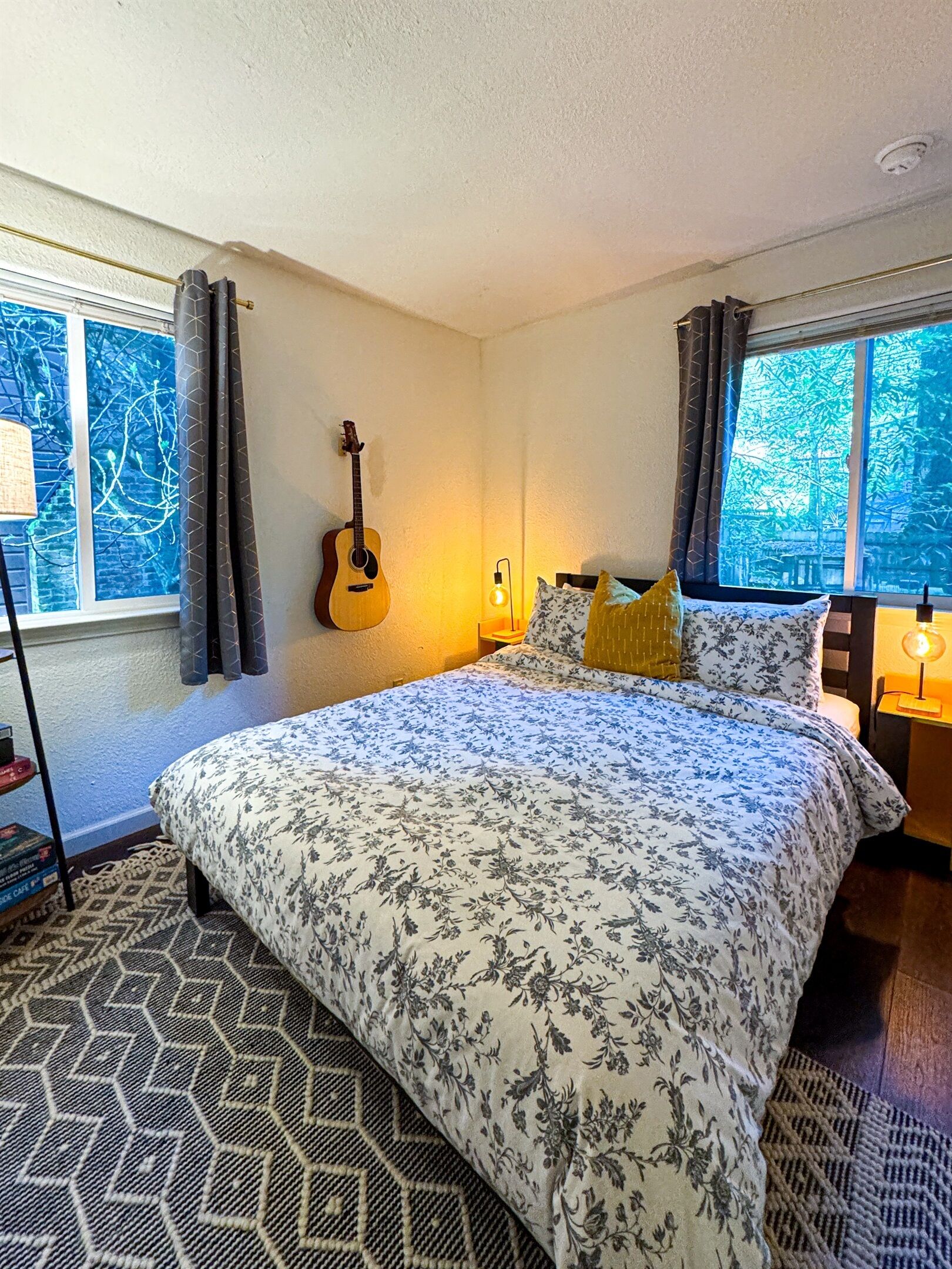 A bedroom with a bed, a guitar, a lamp, and a window with curtains.