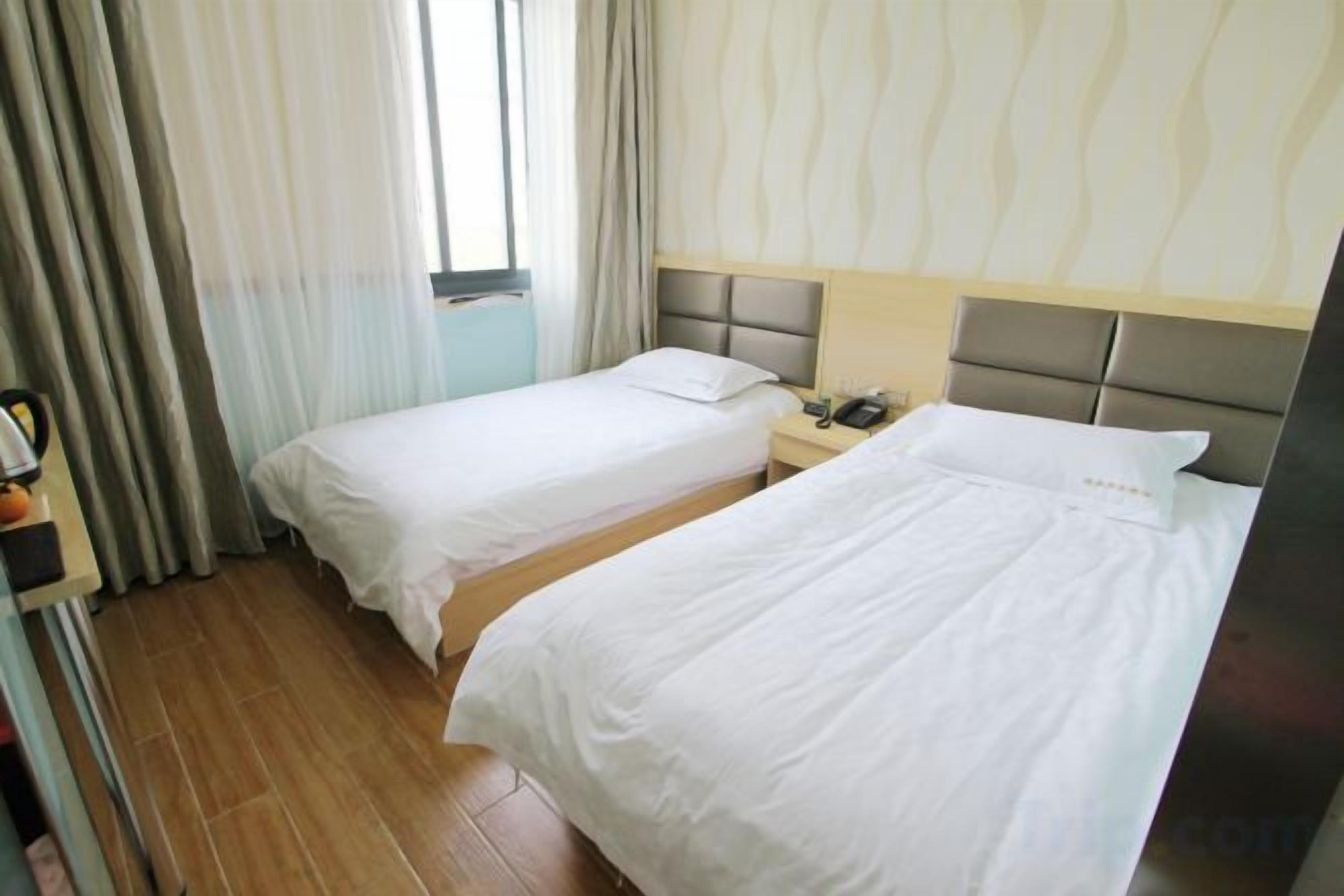 A hotel room with two beds, a bedside table with a lamp, and a window with curtains.